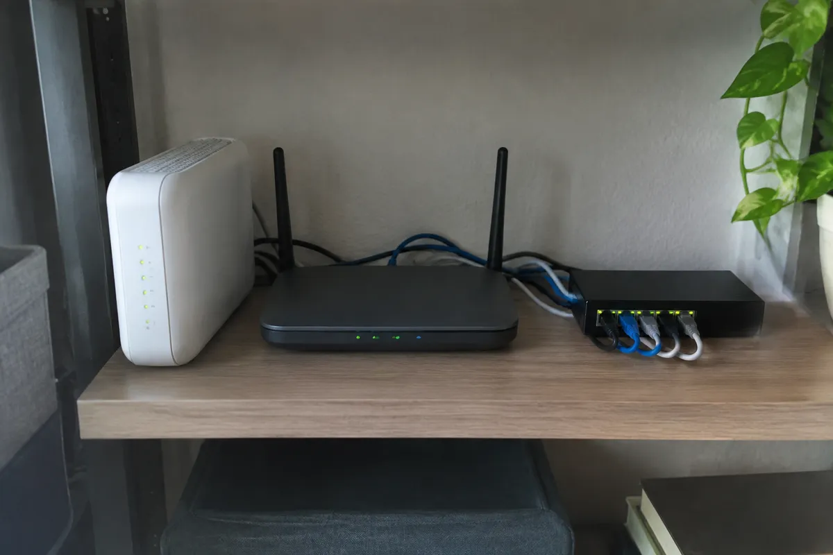a compact home router and modem on a shelf beside a small network switch with a few blinking LEDs and short ethernet cables