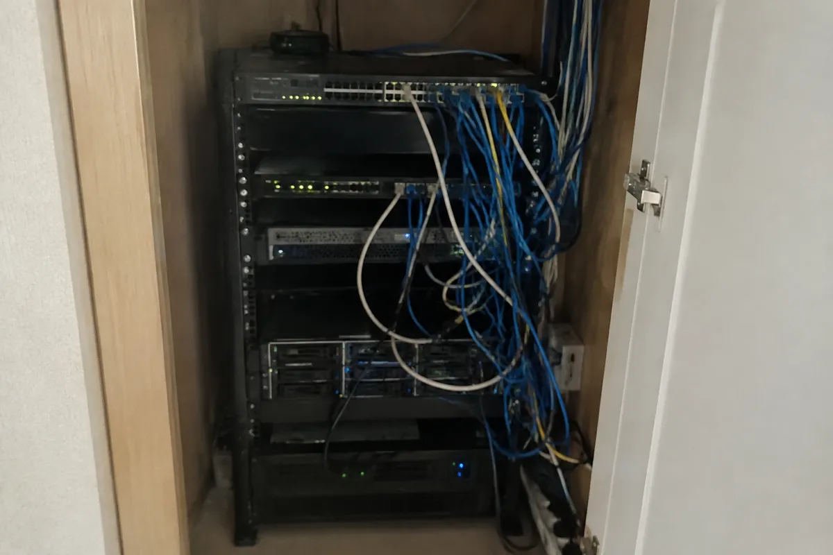 a small server rack in a cupboard with a tangle of cables and a few blinking LEDs