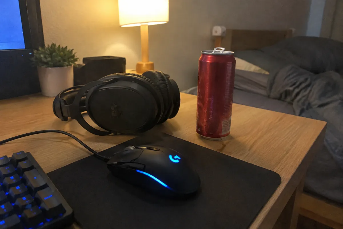 a bedroom desk with a gaming mouse, a headset and a can of soft drink in warm lamp light