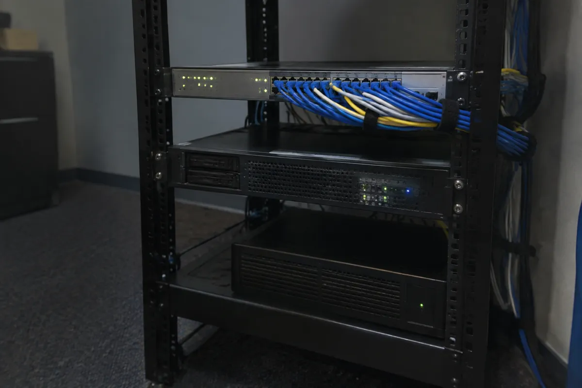a small server rack shelf with a couple of rackmount units and blinking LEDs, neat bundles of cables, dim office
