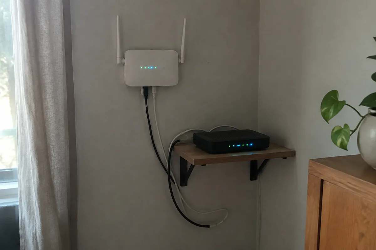 a wall-mounted router and a modem on a shelf with several small LEDs glowing, cables looping down