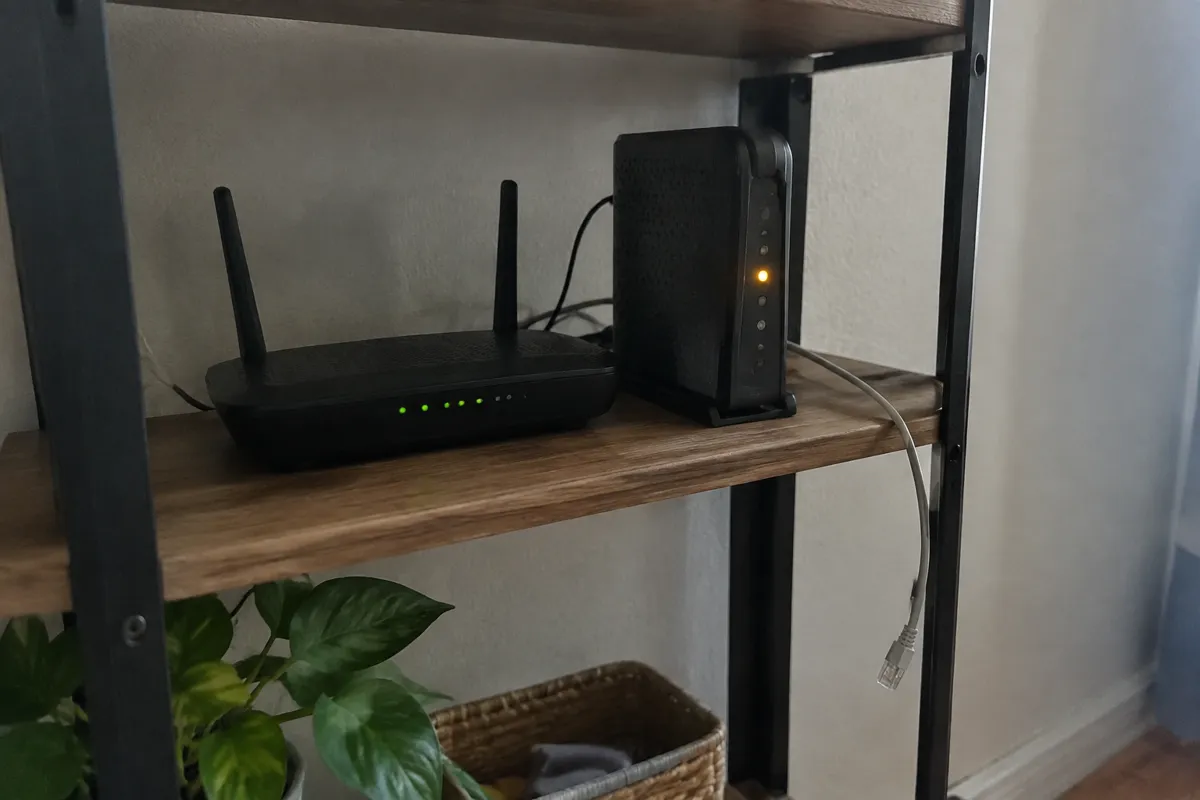 a home router and a modem on a shelf with one amber light blinking and a loose ethernet cable hanging beside them