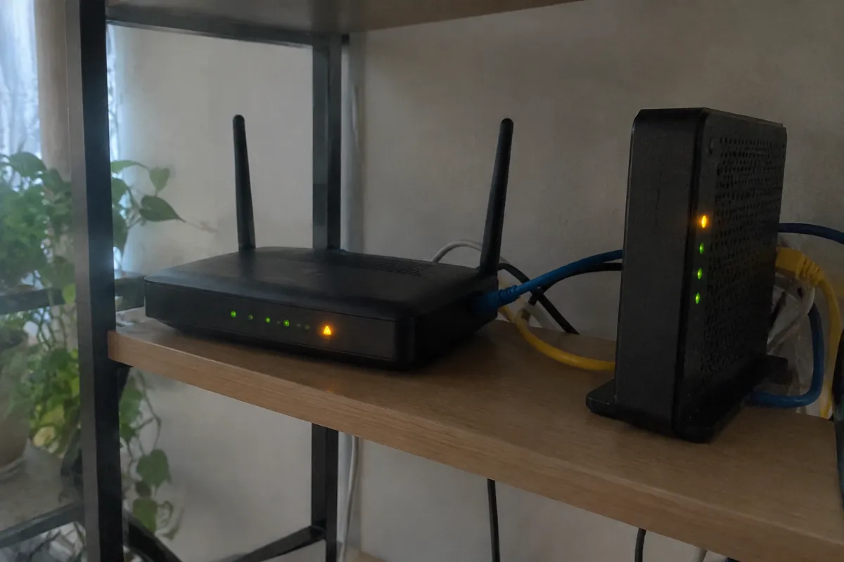 a router and modem on a shelf with an amber warning LED lit and a few loose ethernet cables