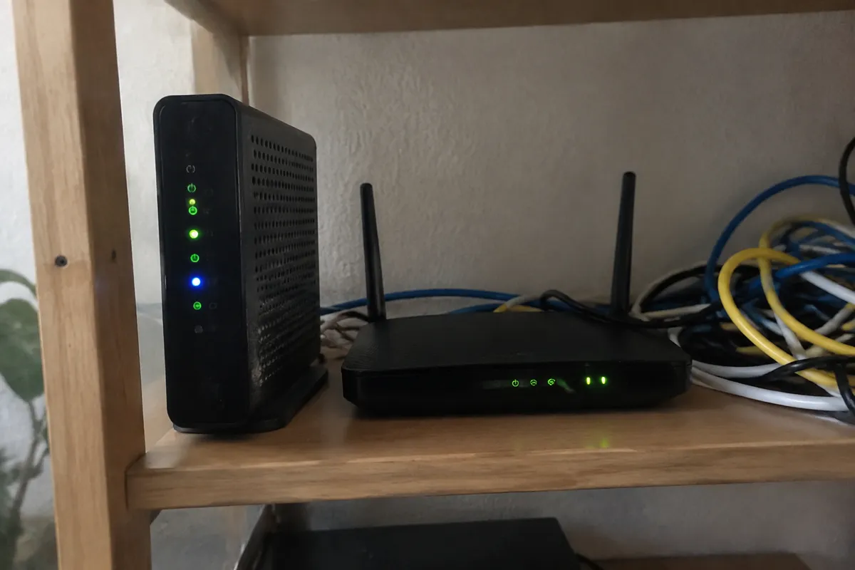 a modem and router on a shelf with a few cables and small glowing LEDs, a tangle of ethernet leads beside them