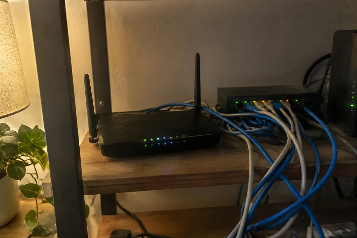 a home router and a tangle of ethernet cables on a shelf, a few LEDs blinking, soft lamp light