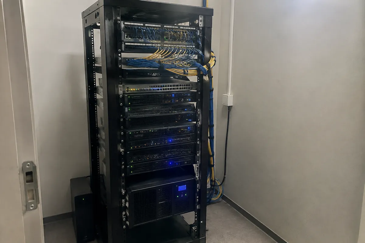 a small server rack with rows of blinking LEDs and bundled cables in a spare room