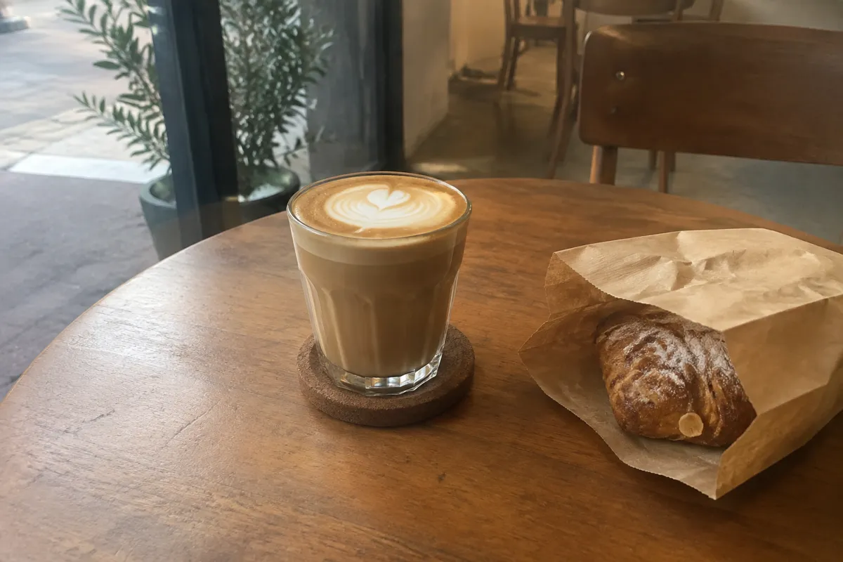 a cafe table with a latte in a glass cup and a small paper bag from a bakery, warm soft light